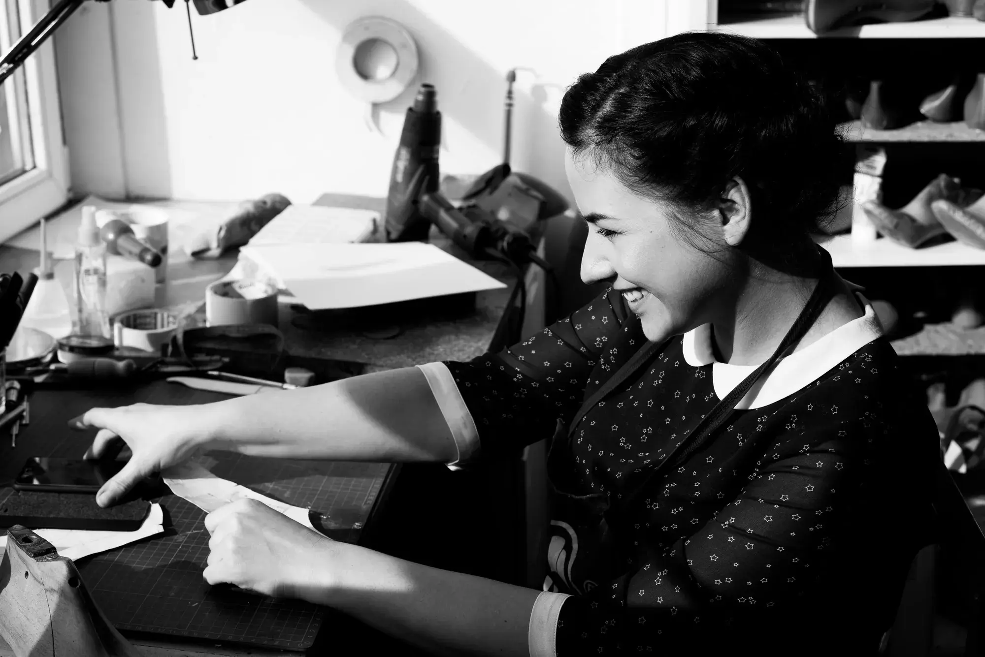 Dana Minkė laughing at the workshop bench as she cuts a paper pattern on the mat, in black and white