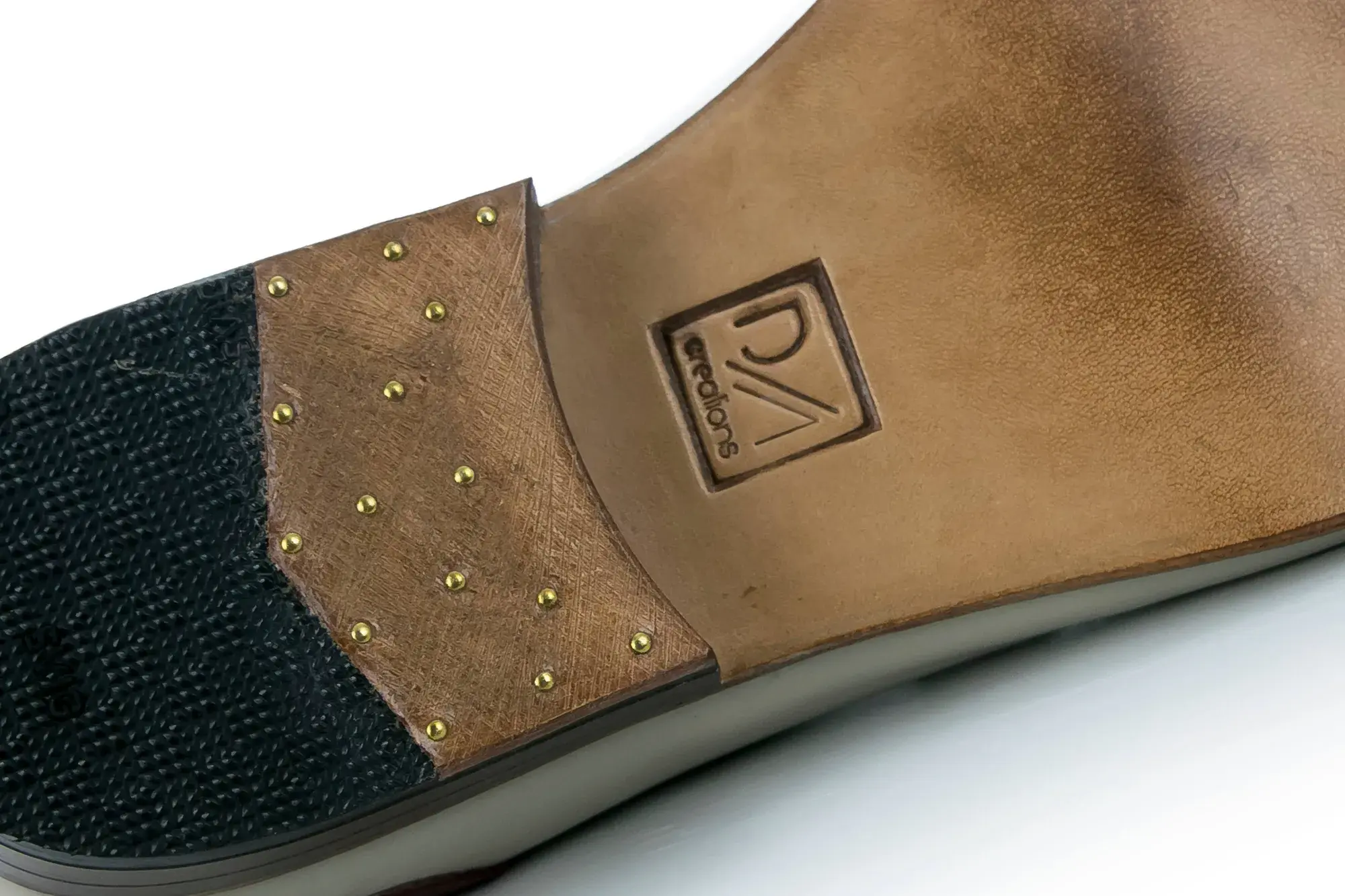 The sole of a stone and burgundy derby, with brass nails and the maker's stamp
