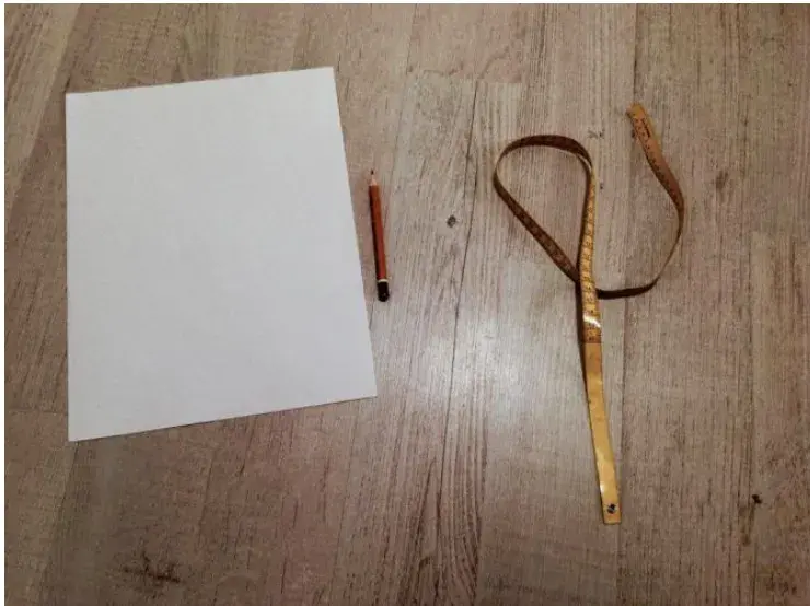 A sheet of paper, a pencil and a folding tape measure laid out on a wooden floor