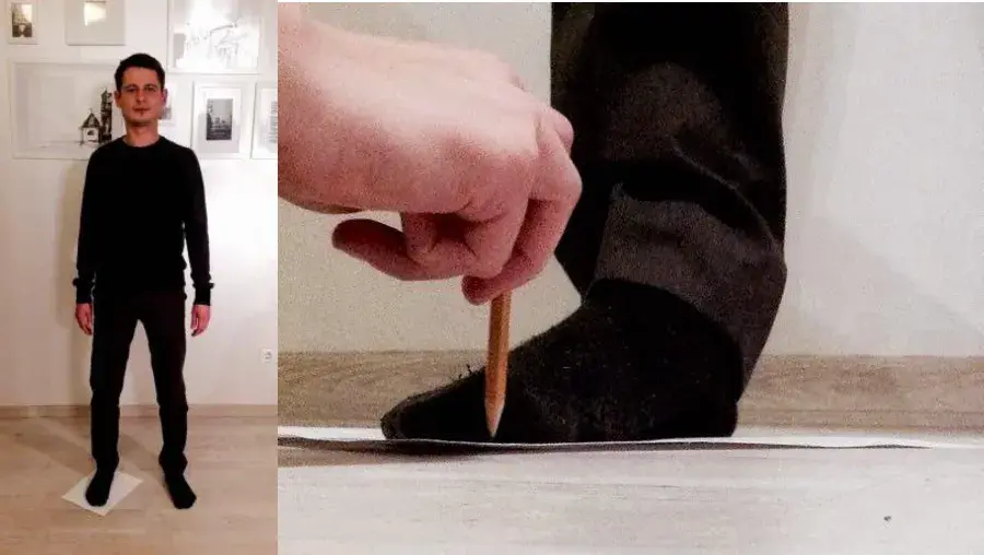 A person standing on a sheet of paper in socks, and a pencil held upright against the foot