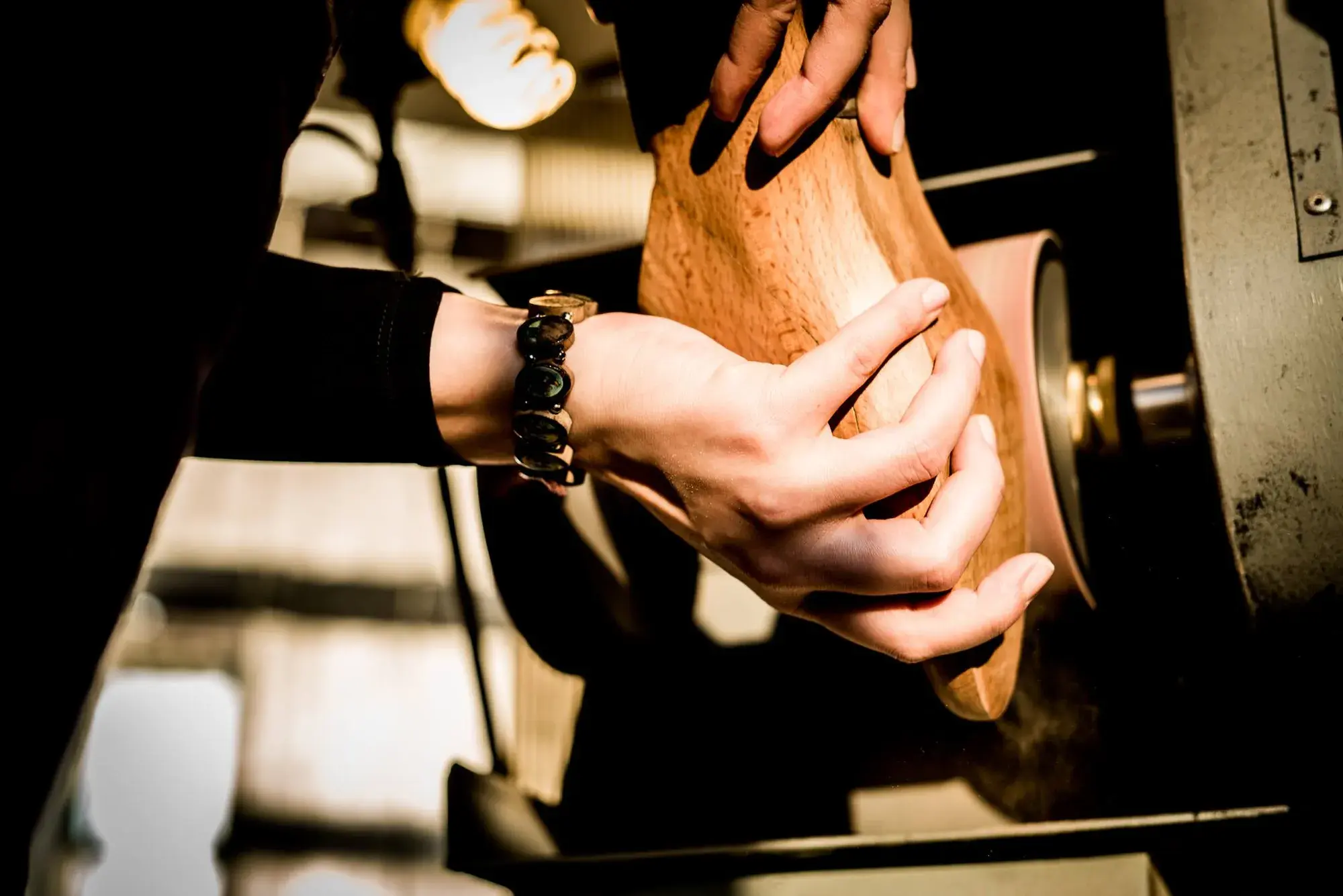 Hands shaping a wooden last against a rotating sanding wheel
