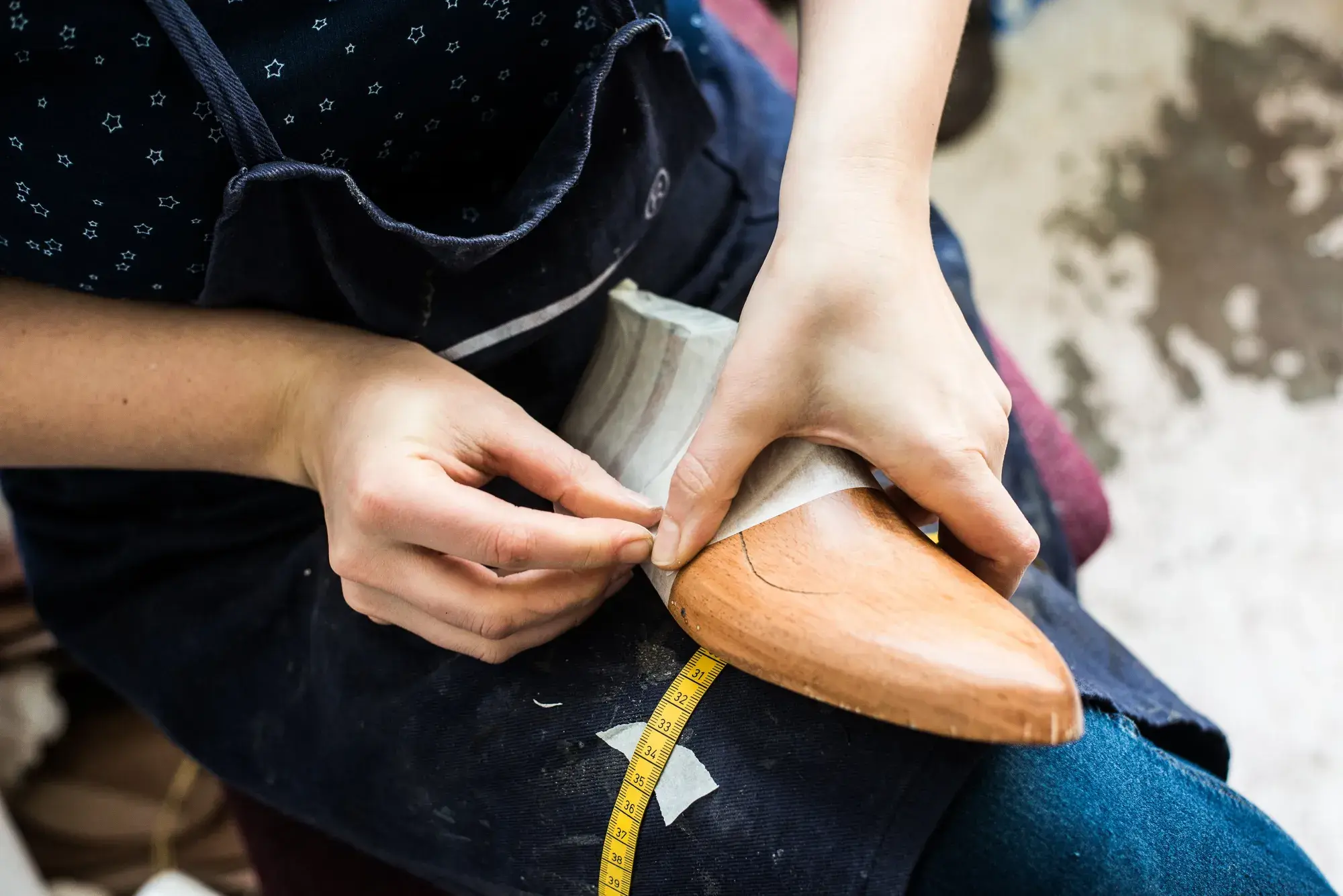 Hands laying the first strips of paper tape on a wooden last, a tape measure across the lap