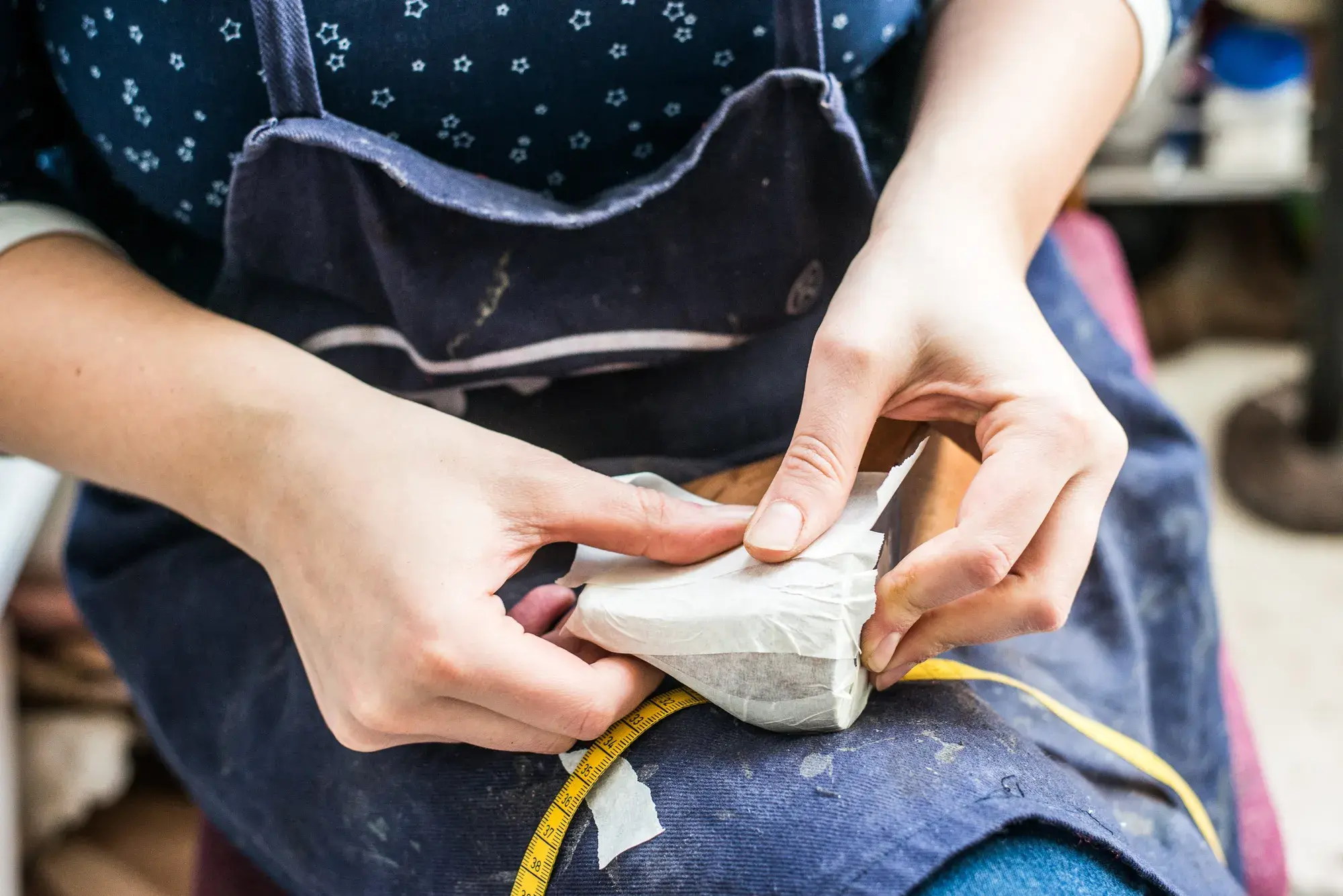 Hands smoothing paper tape over a wooden last, a tape measure across the lap