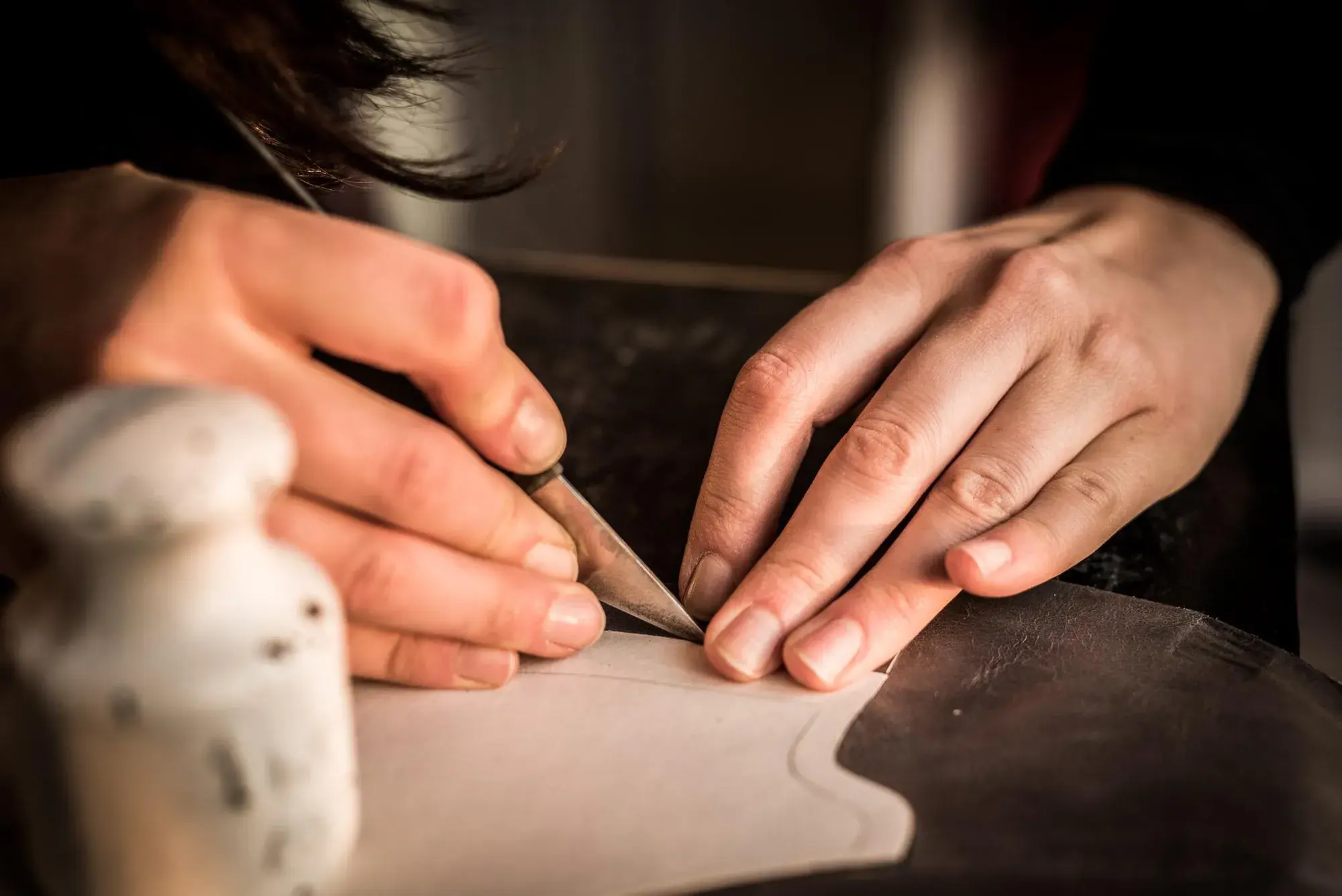 A knife cutting leather around a pattern piece