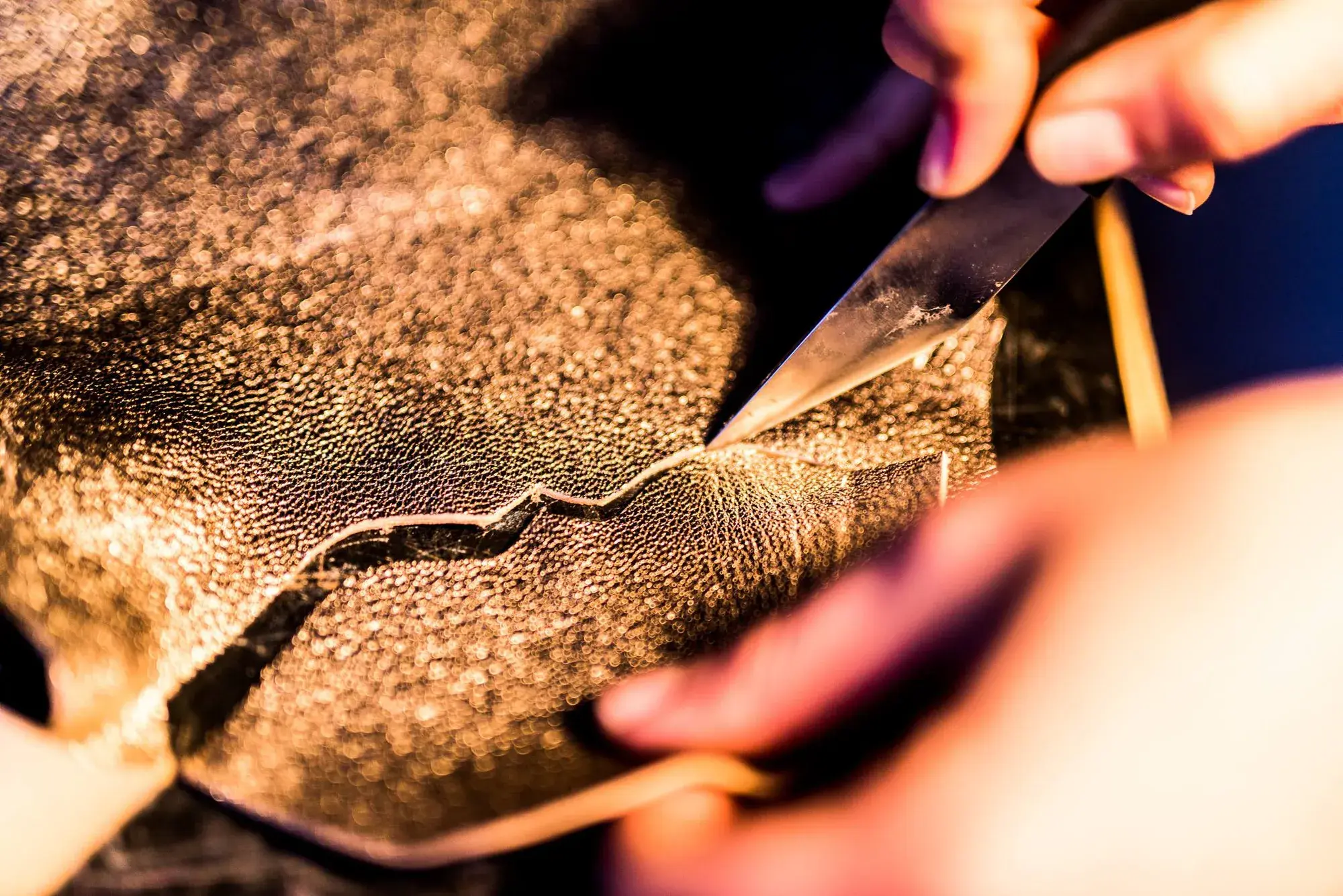 A knife cutting into a textured leather hide
