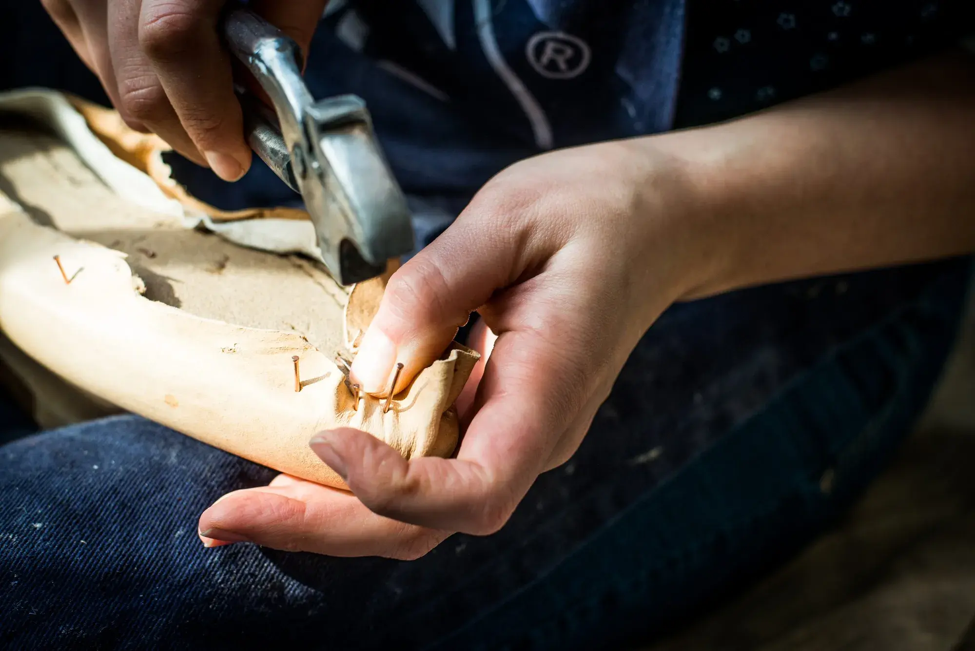 The leather upper being tacked over the wooden last with a lasting hammer