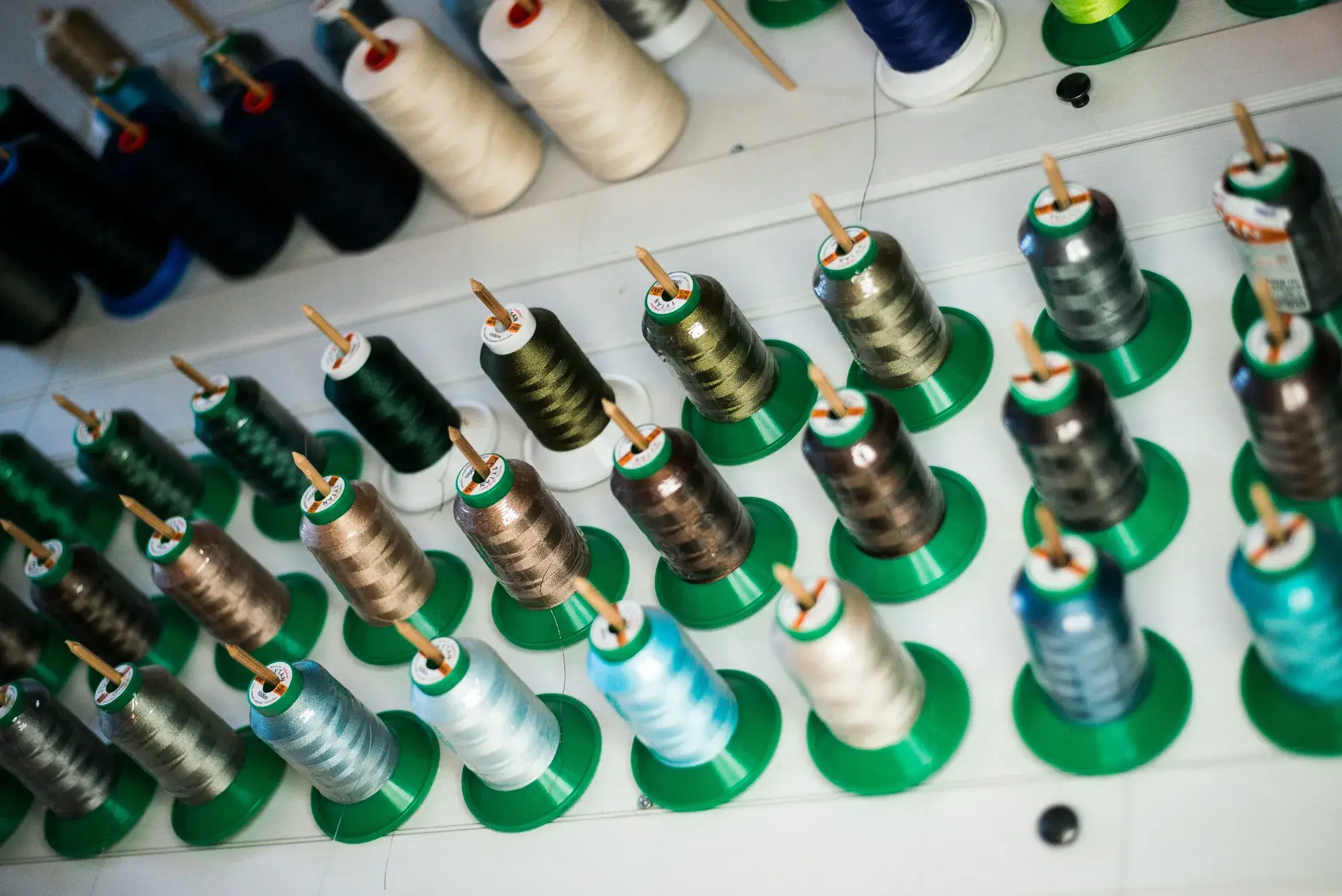 Spools of thread in greens, blues and neutrals on pegs along the workshop wall