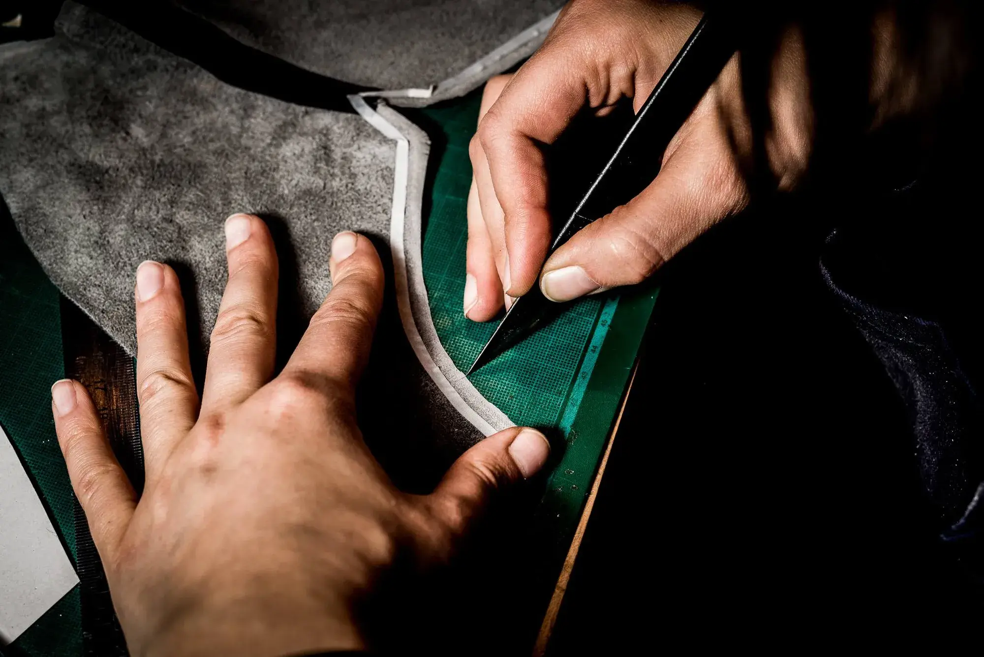 A knife cutting a curved piece of grey leather against a steel rule on the cutting mat