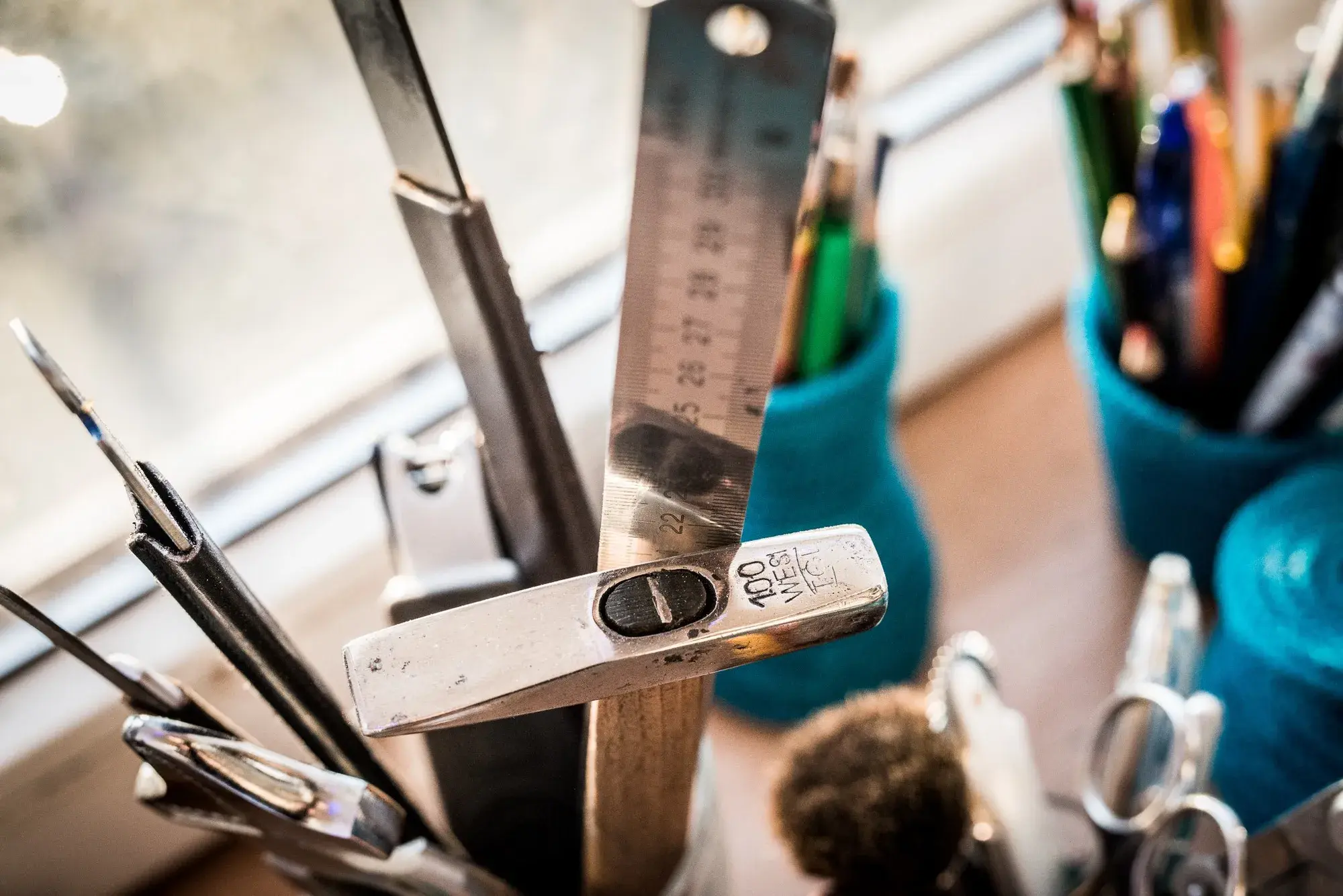 A steel rule, callipers, pencils and scissors standing in pots on the workbench by the window